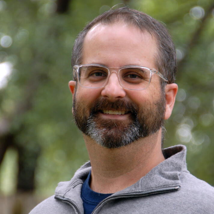 Photo of a man outdoors with a blurry tree in the background